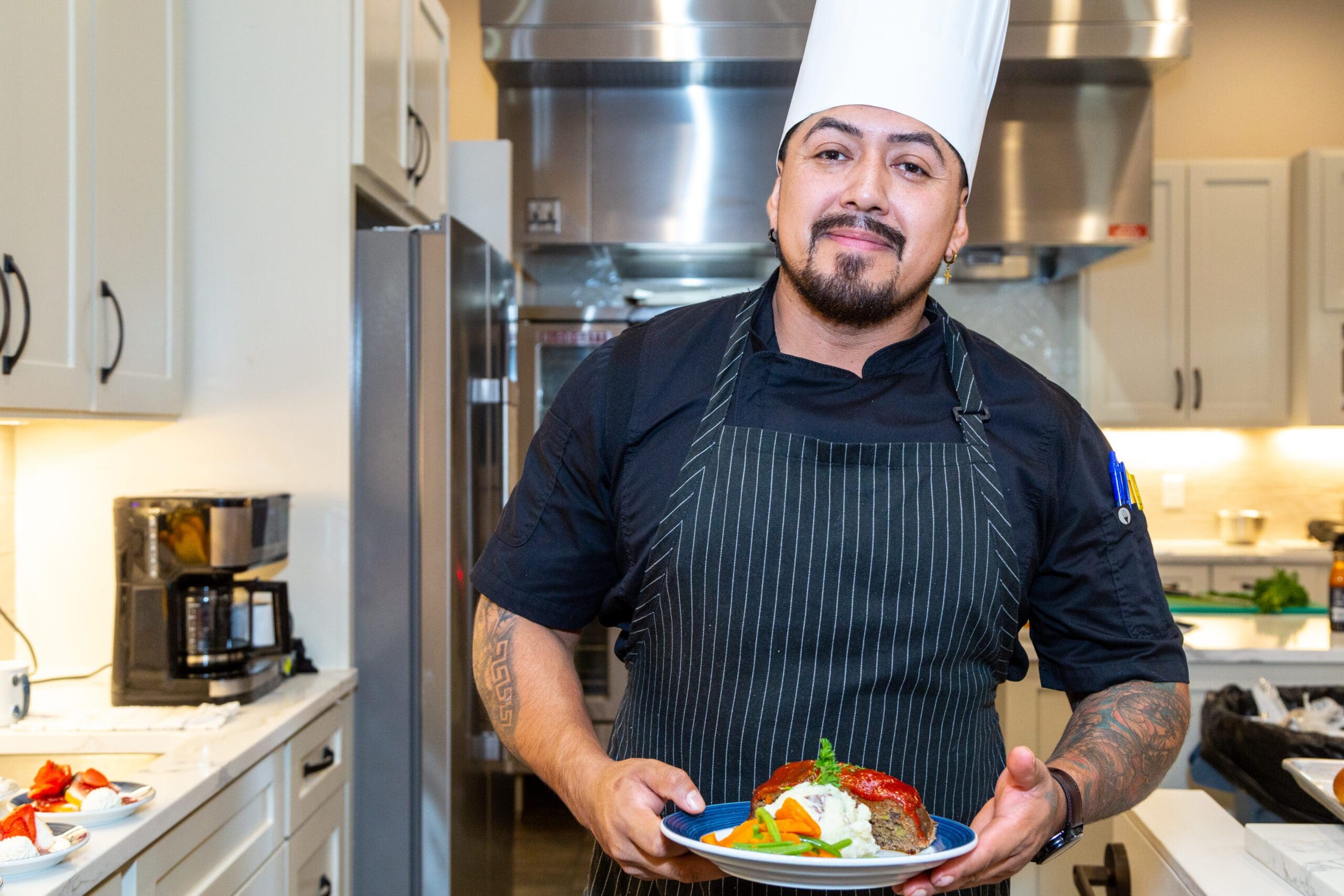 a man wearing a chef hat and apron holding a plate of food