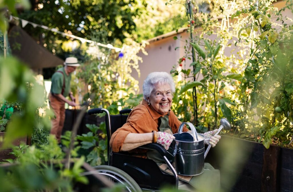  An older adult in a wheelchair holds a watering can while tending to a lush garden.