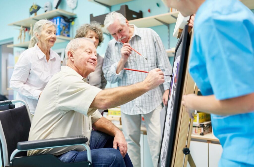 A group of seniors stand around a canvas, each holding a paintbrush to work on a painting together in assisted living