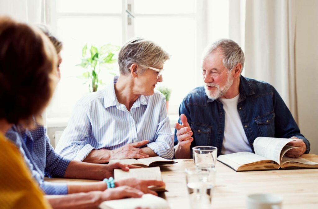 Four seniors sit around a table in a memory care community with several copies of the same book to discuss together