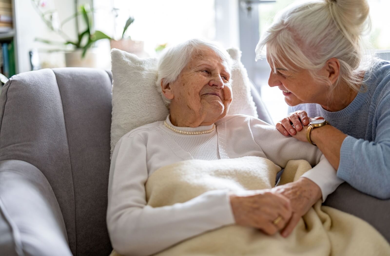 Adult child having a conversation with their senior parent, who is sitting on a chair with a blanket.