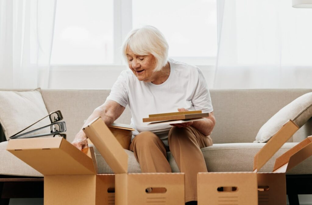 A senior sits on a sofa surrounded by boxes while organizing their belongings, preparing to move into memory care.