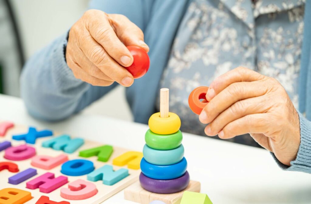 A senior with Alzheimer’s practices fine motor skills using colorful children’s toys at a memory care community