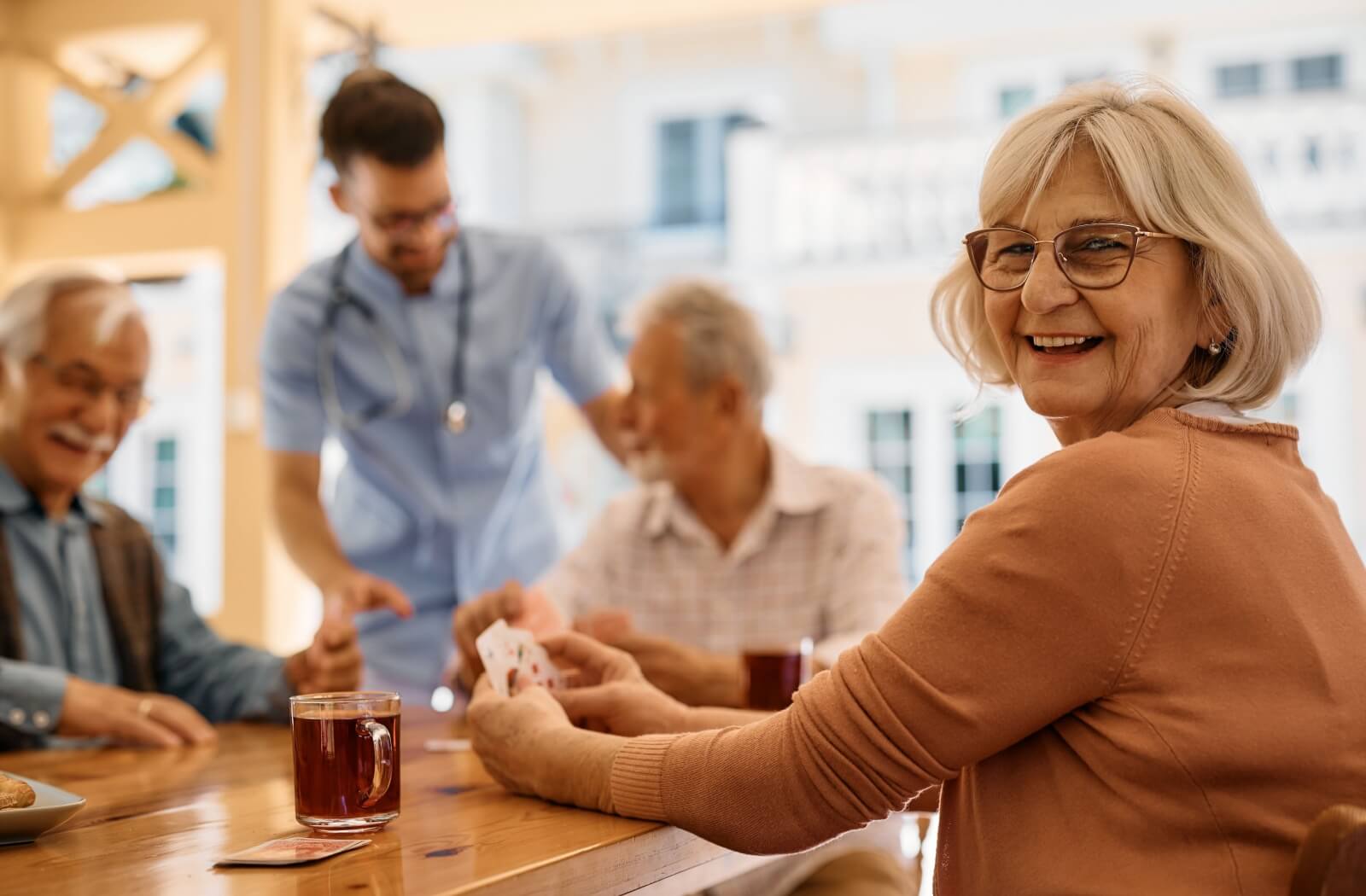 An assisted living resident smiles as they enjoy a game of cards with fellow residents.