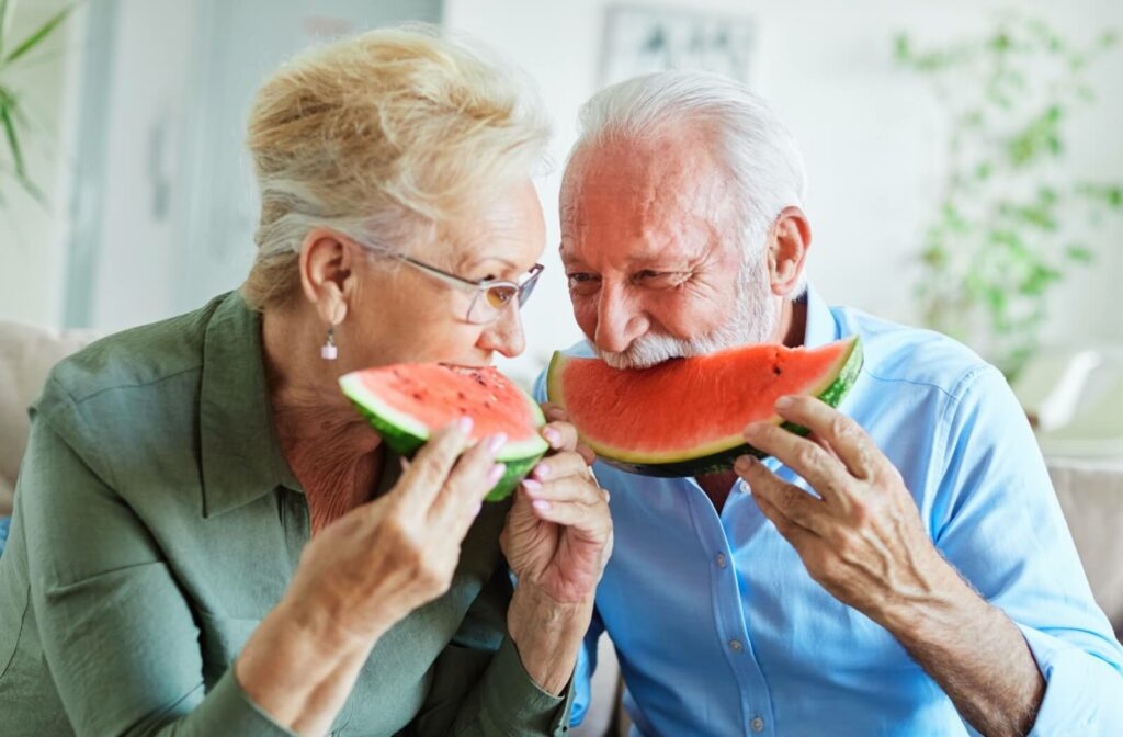 A senior couple giggle while eating watermelon for a summer afternoon snack to bolster their hydration