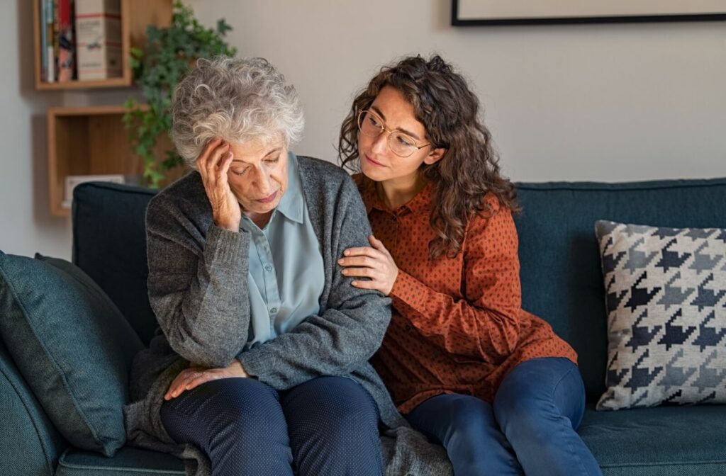 A young adult hugs their stressed grandparent while sitting together on a couch in memory care