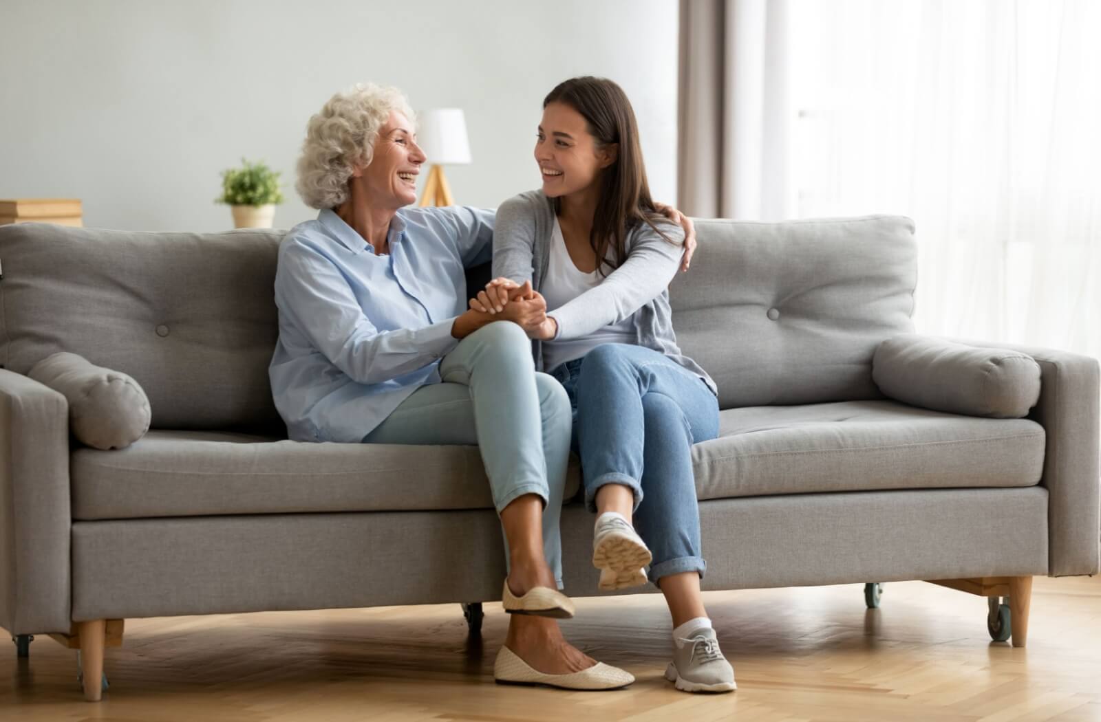 An adult child talks and holds hands with their parent with dementia while sitting on a couch together.