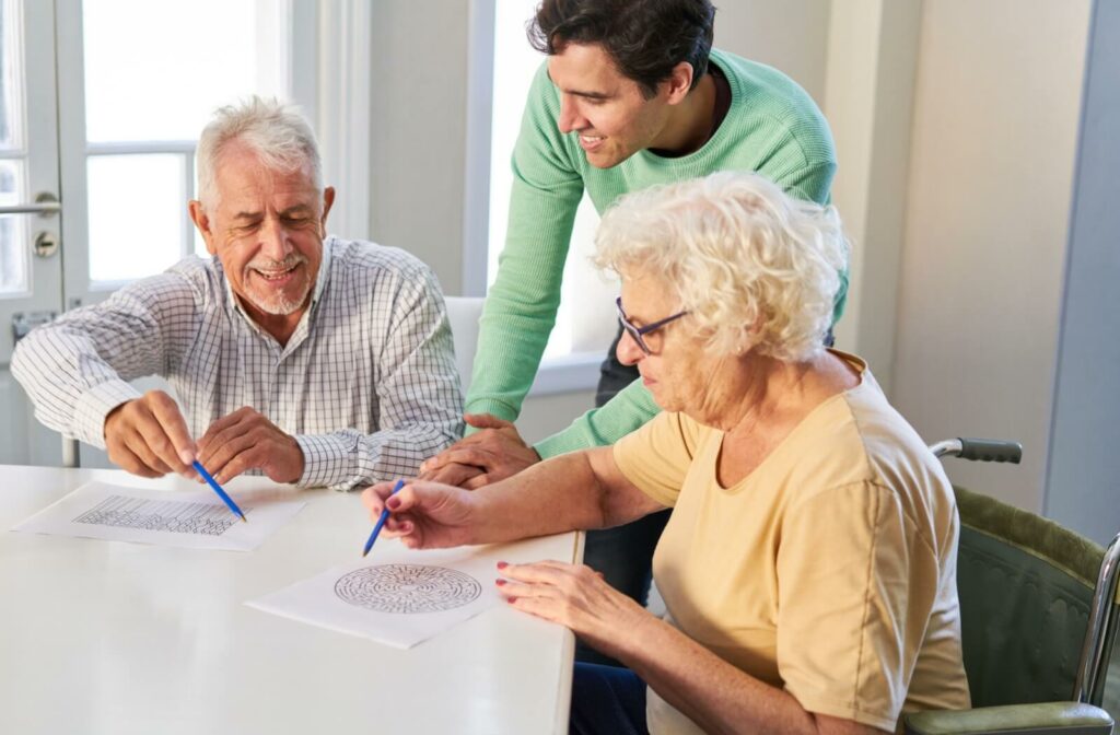 Older man and woman doing puzzles on a table while younger man watches between them.