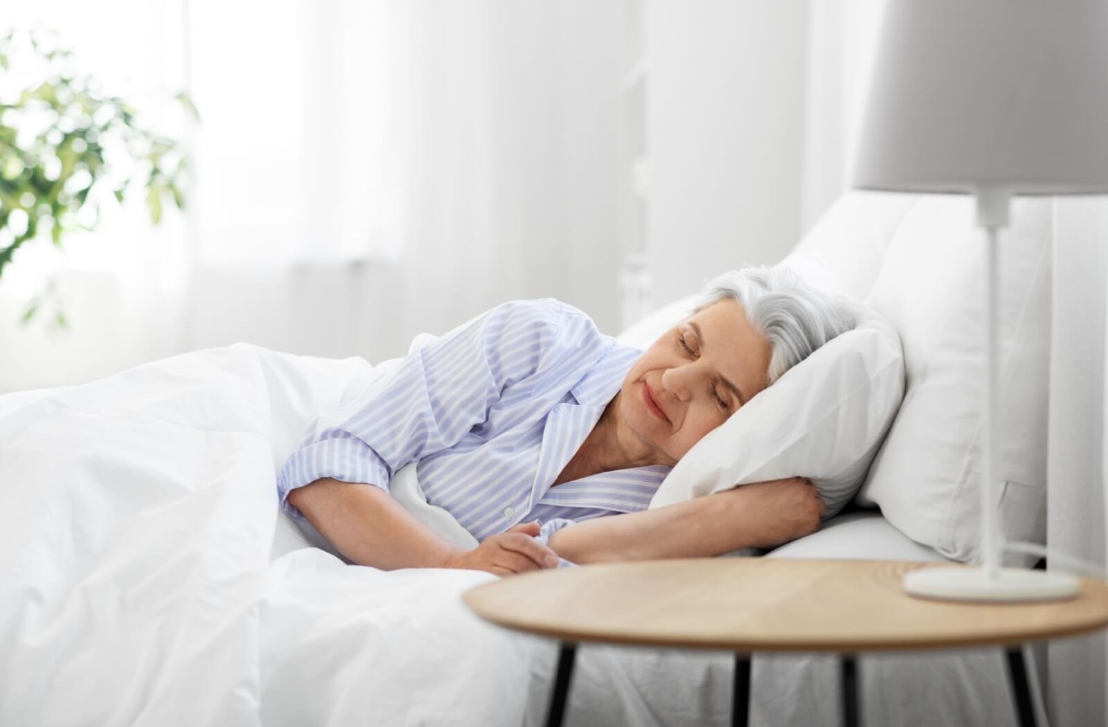A senior laying in bed on their side and sleeping peacefully.