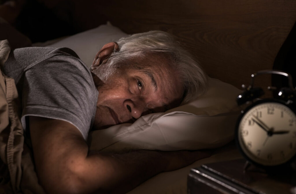 A senior lying in bed looking exhausted while staring at their bedside clock