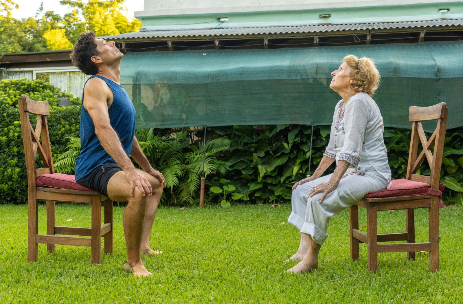 A senior resident participates in an outdoor chair yoga class with younger yoga instructor.
